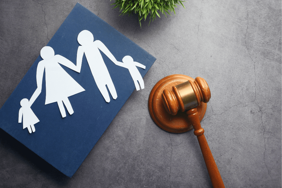A symbolic representation of family law on a gray background, featuring a paper cutout of a family consisting of two adults and two children next to a wooden judge's gavel.
